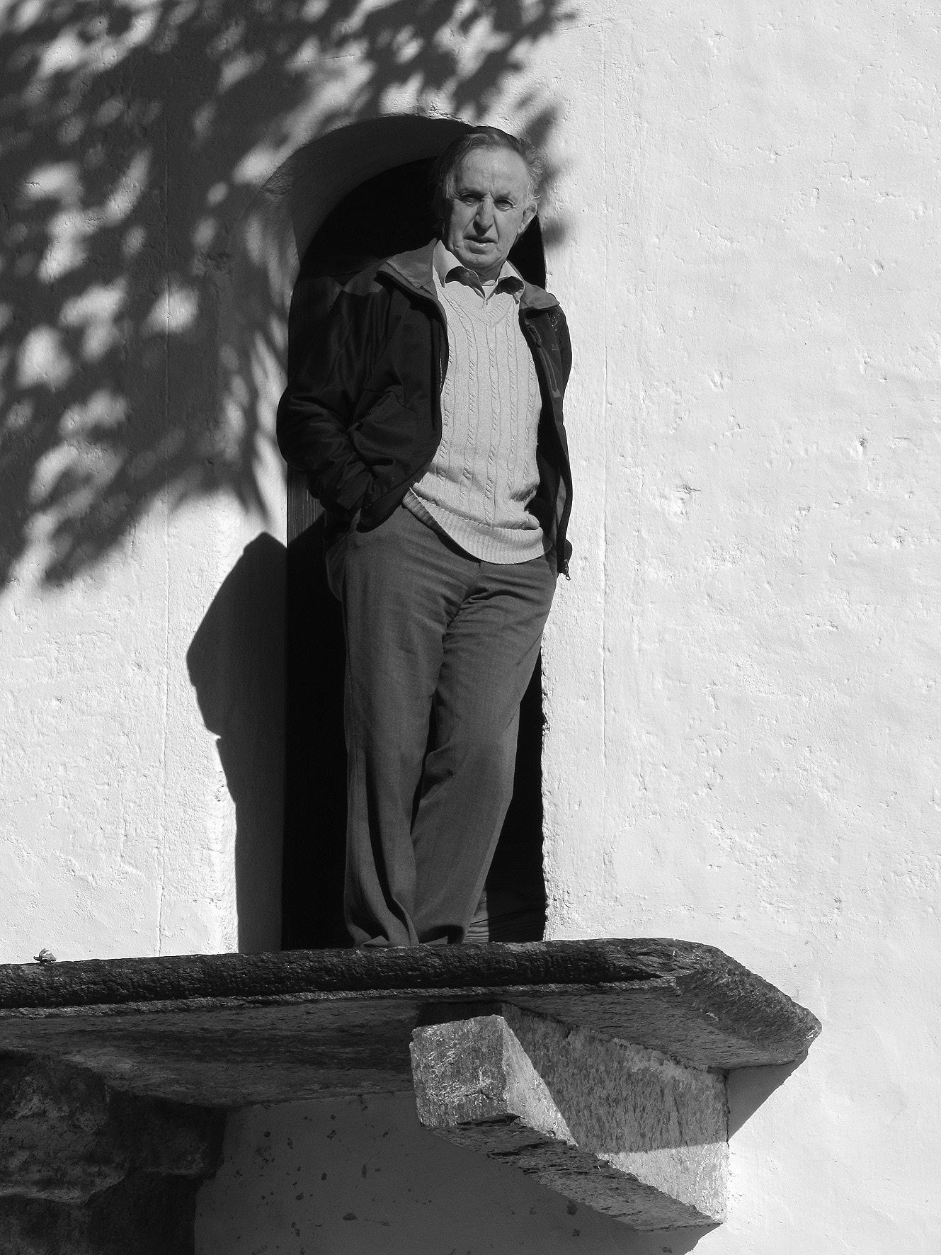 Herbert Rauch steht in einer Nische einer weißen Mauer, darüber Blattschatten