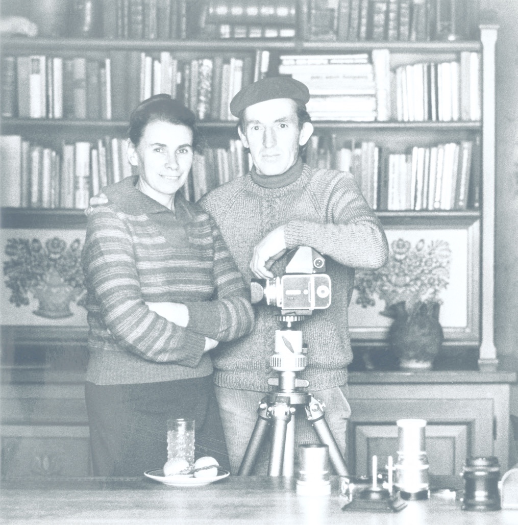 Herbert und Maria Rauch vor einem Bücherregal, davor eine Kamera auf einem Stativ